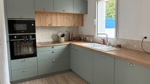 Une cuisine avec des meubles gris, un plan de travail en bois, un four encastré et une fenêtre laissant entrer la lumière naturelle.