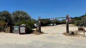 Une entrée fermée par une barrière, un panneau et un petit bâtiment.