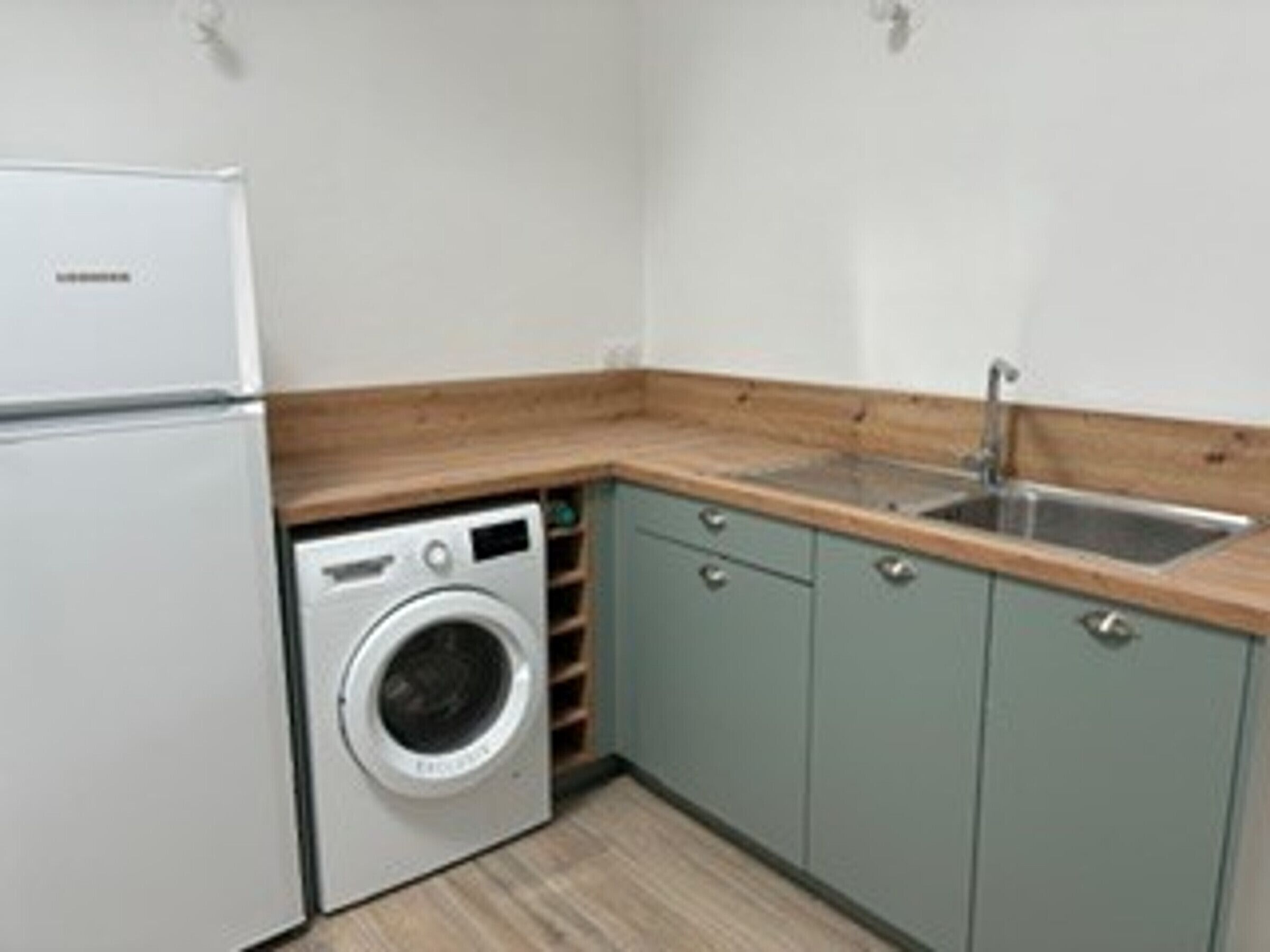 A compact kitchen with a washing machine, a sink, and light-colored cabinets.
