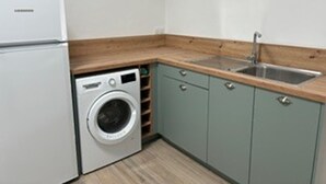 Une cuisine de taille réduite, équipée d’un lave-linge, d’un évier et de meubles de couleur claire.