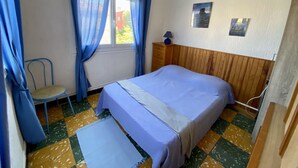 Quarto com cama, cadeira, janela com cortinas, luminária na parede e um quadro.