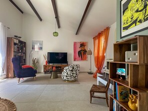 Ein Wohnzimmer mit Fernseher, Bücherregal, Sessel, Couchtisch und einem weiteren Bücherregal mit Büchern und Dekoration.