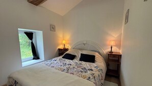 Ein Schlafzimmer mit einem Bett, zwei Nachttischlampen, einem Fenster mit Vorhang und einem Bild an der Wand.