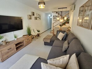 A modern living room with a flat-screen TV, a wooden entertainment unit, a grey sofa, and a staircase leading to an upper level. - Duplex pets welcome - central location (Llançà)