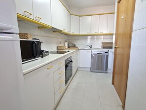 A compact kitchen with white cabinets, a microwave, a dishwasher, and a wooden door. - Duplex pets welcome - central location (Llançà)