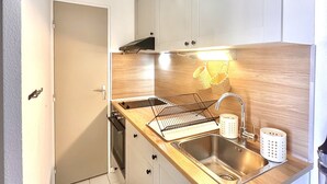Une cuisine compacte avec des meubles blancs, un plan de travail en bois, un évier en acier inoxydable et un four encastré.