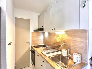 Eine kompakte Küche mit weißen Schränken, einer Holz Arbeitsplatte, einem Edelstahl-Spülbecken und einem eingebauten Backofen.