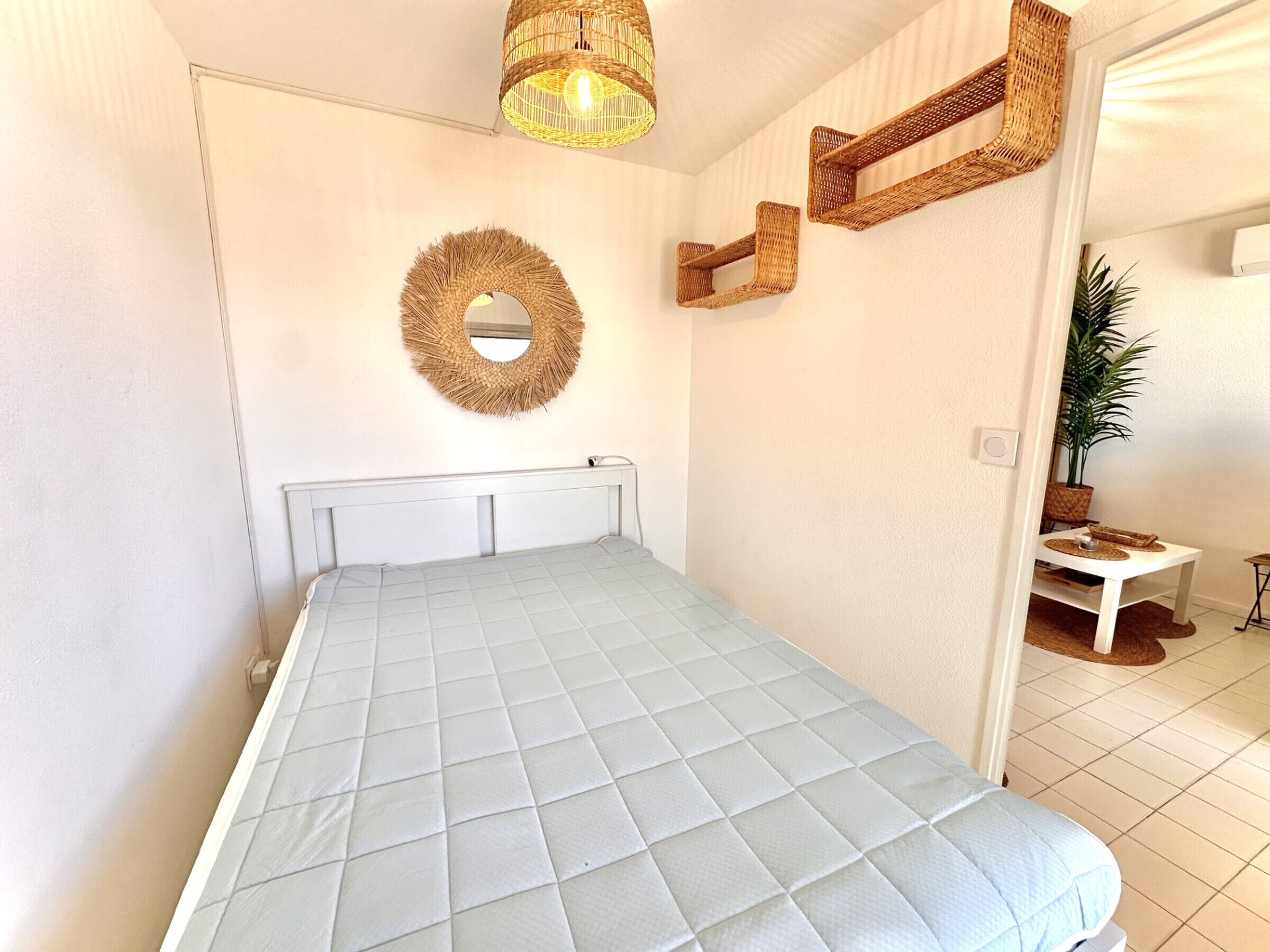 A bedroom with a bed, a wall-mounted mirror, and wicker wall shelves.