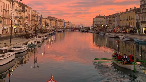 Une vue urbaine sur le front de mer, avec des bâtiments, une rivière paisible et un bateau transportant des passagers.