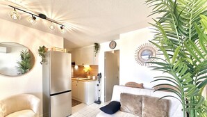 Un salon moderne avec un canapé, un fauteuil, un grand miroir et une cuisine en arrière-plan.
