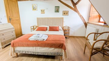 Une chambre avec un plafond en bois, un lit recouvert d’une courtepointe blanche et orange, une commode en bois et une chaise en osier.