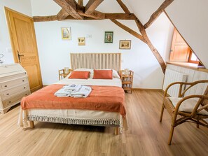 Une chambre avec un plafond en bois, un lit recouvert d’une courtepointe blanche et orange, une commode en bois et une chaise en osier.