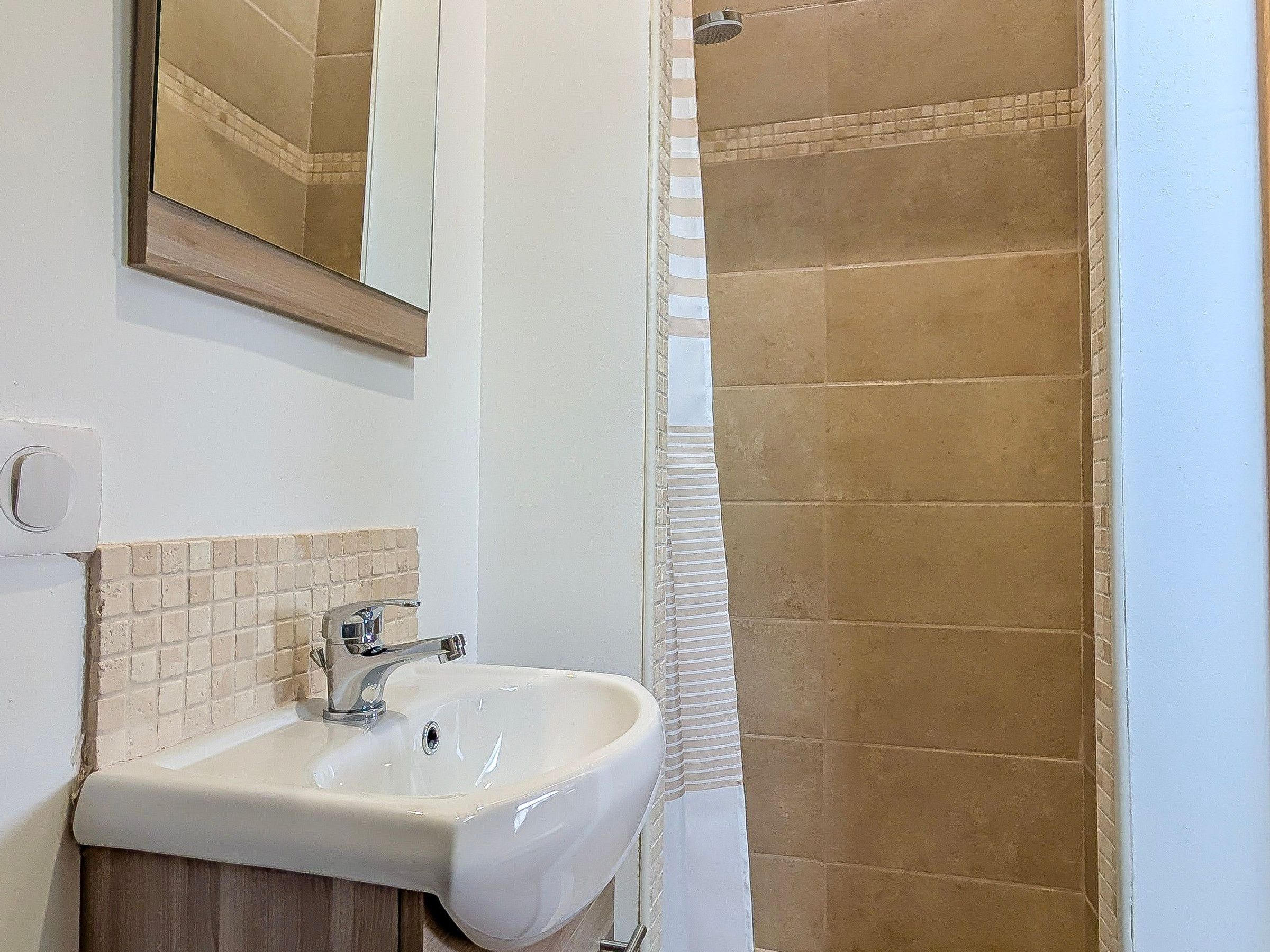 A bathroom with a sink, mirror, and shower.