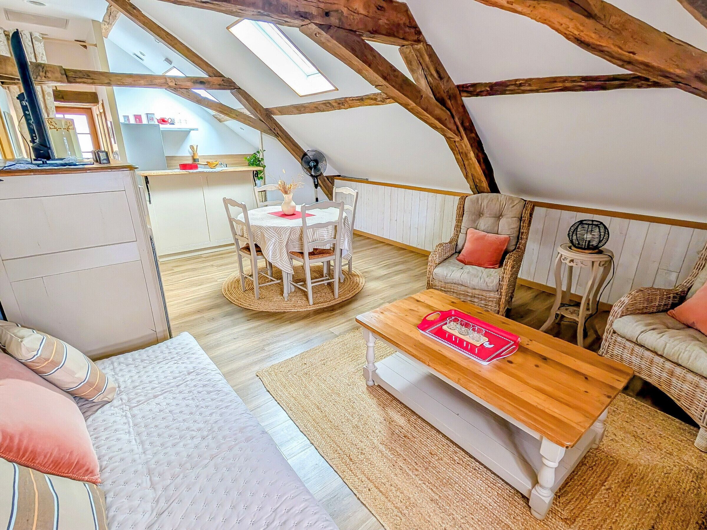 A cozy loft bedroom with a high ceiling, a dining area with a round table, and a seating area with a sofa and armchairs.