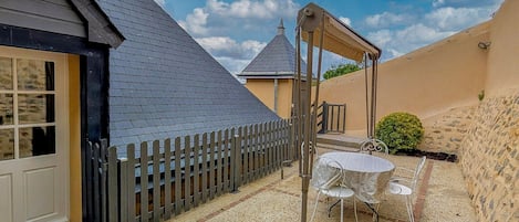 A courtyard with a patio table and chairs, a wooden fence, and a building with a dark roof and beige walls.