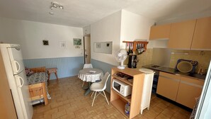 Een kleine keuken met een eettafel, stoelen, een koelkast en een magnetron.