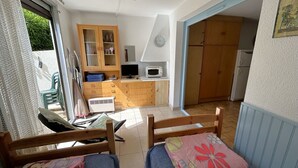 Een kamer met een bed, een klein bureau, een stoel, een kitchenette en een deur naar een andere kamer.