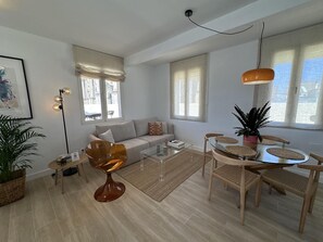 A modern living room with a sofa, coffee table, dining table with chairs, a floor lamp, and large windows. - Penthouse with panoramic cathedral view - 6 guests (Málaga)