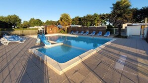 Ein rechteckiger Swimmingpool mit einer Rutsche, umgeben von Liegestühlen und Palmen.