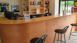 Eine Bar mit einer Theke, Hockstühlen und Regalen voller Flaschen und Gläsern.