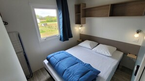 Ein Schlafzimmer mit Bett, Vorhängen am Fenster, einem Kopfteil, Nachttischlampen und einem Holzregal.