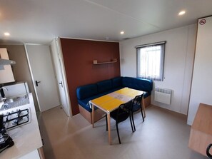 Eine kleine Küche mit Herd, einem Esstisch mit Stühlen, einem blauen Sofa und einem Fenster mit Vorhängen.