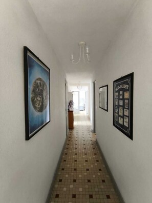 Ein Korridor mit Fliesenboden, gerahmten Kunstwerken an den Wänden und einer Chandelier.