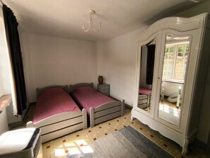 Une chambre avec deux lits, une armoire, un miroir et un radiateur.