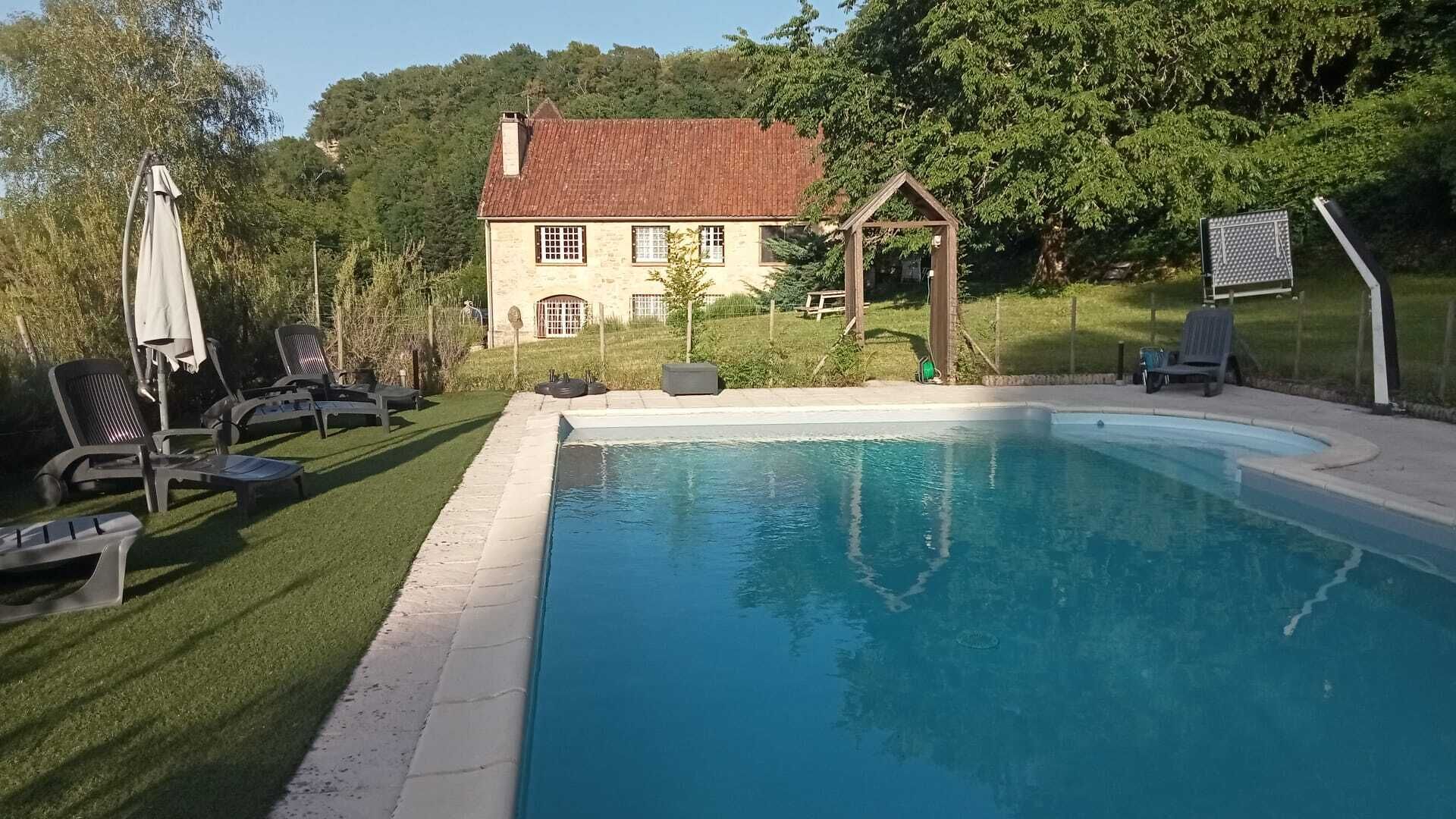 A swimming pool with a house in the background, surrounded by a fenced yard with lawn chairs.