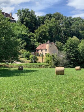 A stone house with a red roof surrounded by lush greenery and hay bales in a field. - 10 km south of Sarlat, first floor of a Périgord-style house (Sainte-Mondane)