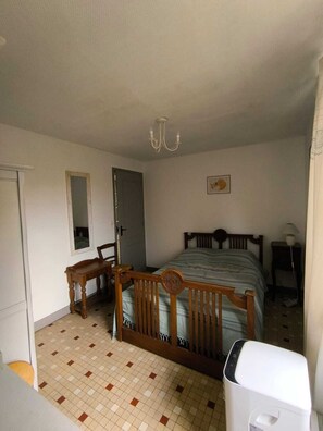 A bedroom with a wooden bed, a chair, a bedside table, a mirror, a door, and a white radiator. - 10 km south of Sarlat, first floor of a Périgord-style house (Sainte-Mondane)