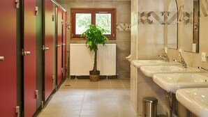 A hotel bathroom with multiple sinks, a radiator, a potted plant, and lockers.