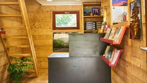 A wooden cabin interior with a desk, bookshelves, a ladder, and a window.