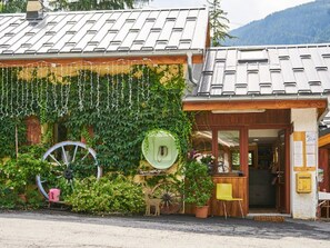 A rustic building with a green ivy-covered wall, a large wheel, and a wooden door. - Cozy chalet, pets allowed - 5 guests (Séez)