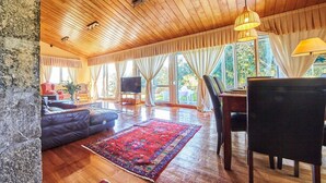 A spacious living room with a wooden ceiling, large windows, a sofa, a TV, and a dining area. - Rural Charm Near the Sea: Casa Íntegra in Ajo (Bareyo)