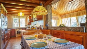 A kitchen with wooden cabinets, a washing machine, and a dining table set with plates, glasses, and a loaf of bread. - Rural Charm Near the Sea: Casa Íntegra in Ajo (Bareyo)