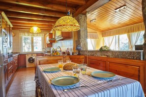 A kitchen with wooden cabinets, a washing machine, and a dining table set with plates, glasses, and a loaf of bread.