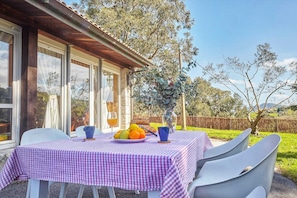 An outdoor dining area with a checkered tablecloth, chairs, a vase with flowers, and a view of the surrounding landscape.