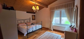 A bedroom with a bed, a chandelier, a window with curtains, and a radiator.