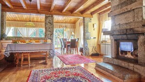 A rustic interior with a stone fireplace, wooden beams, a dining area with a table and chairs, and a view through a window. - Rural Charm Near the Sea: Casa Íntegra in Ajo (Bareyo)