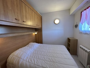 Ein Schlafzimmer mit einem hölzernen Kopfteil, einem Einzelbett, einem Nachttisch, einem Heizkörper und einem Fenster mit Vorhang.