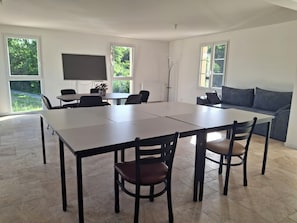 A modern dining area with a large table and chairs, a sofa, and a TV screen.