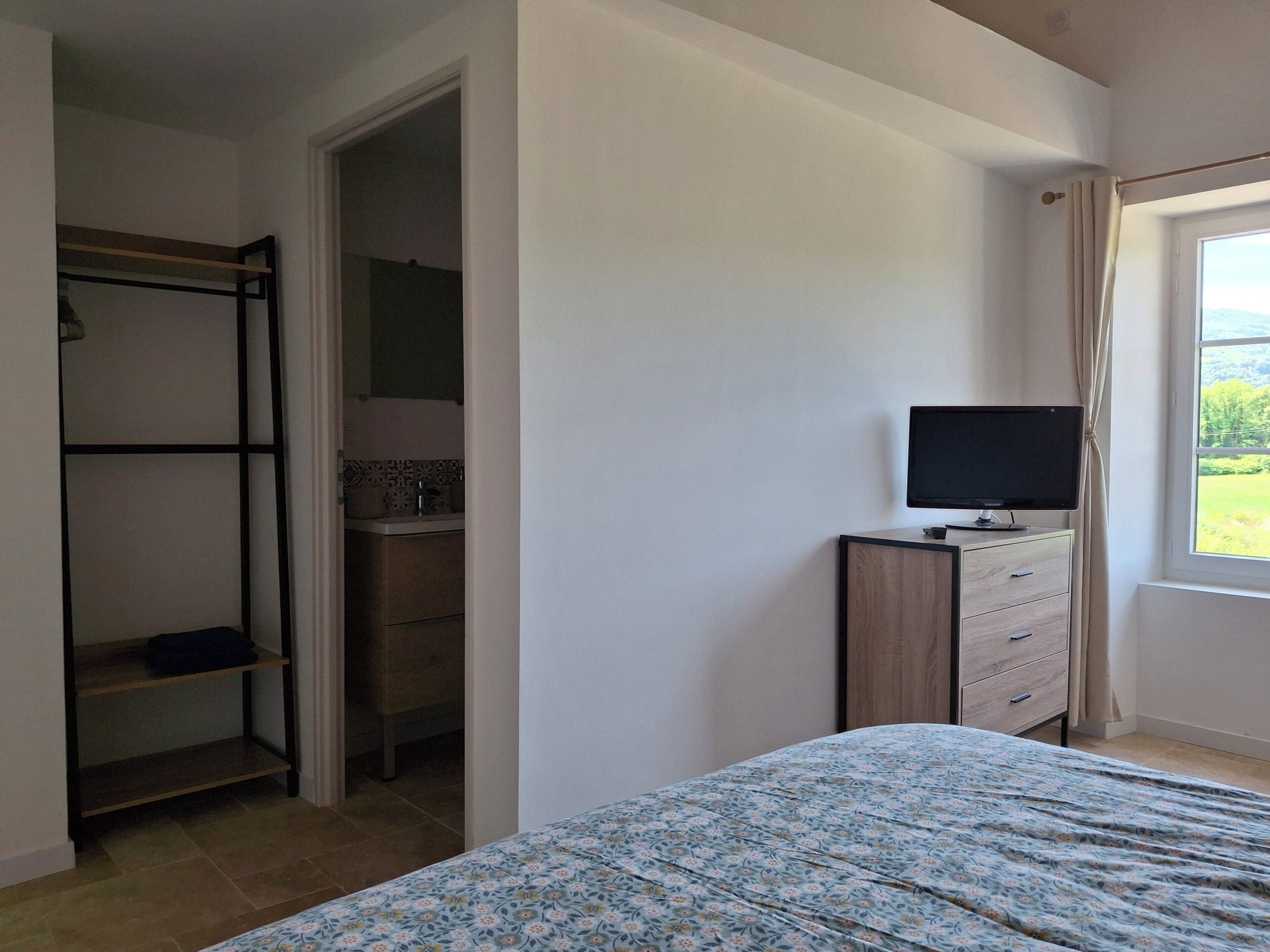 A bedroom with a bed, a TV on a stand, a wardrobe, and a window with a view.