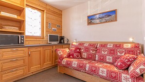 Ein gemütliches Zimmer mit Holzwänden, einer Couch mit gemusterten Kissen, einem Fernseher, einer Mikrowelle und einer Kaffeemaschine.