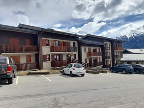 En byggnad med flera våningar, balkonger, en parkeringsplats och en bergig bakgrund.