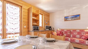 Ein Essbereich mit Tisch für vier Personen, eine Küchenzeile mit Mikrowelle und Kaffeemaschine sowie ein rotes, gemustertes Sofa.