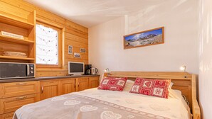 Ein Schlafzimmer mit einem Bett, Holzschränken, einem Fernseher, einer Kaffeemaschine und einem gerahmten Bild an der Wand.