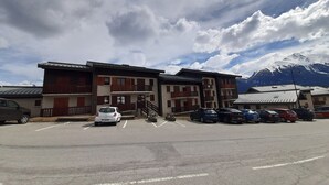 Ein mehrgeschossiges Gebäude mit Parkplatz davor, einer Treppe, die zum Eingang führt, und schneebedeckten Bergen im Hintergrund.