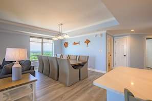 Ein modernes Wohnzimmer mit Essbereich, einer Couch, einer Lampe und Blick durch das Fenster.