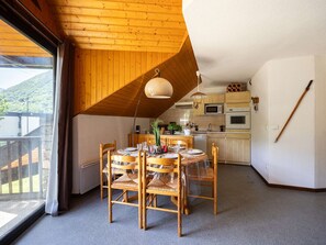 Ein Essbereich mit Holztisch und Stühlen, eine Küche mit Geräten sowie Blick auf eine gebirgige Landschaft.